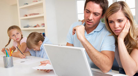 couple struggling over bills using laptop with children nearby