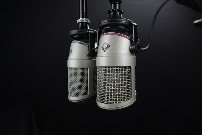Two professional looking microphones hanging from booms on a grey background.