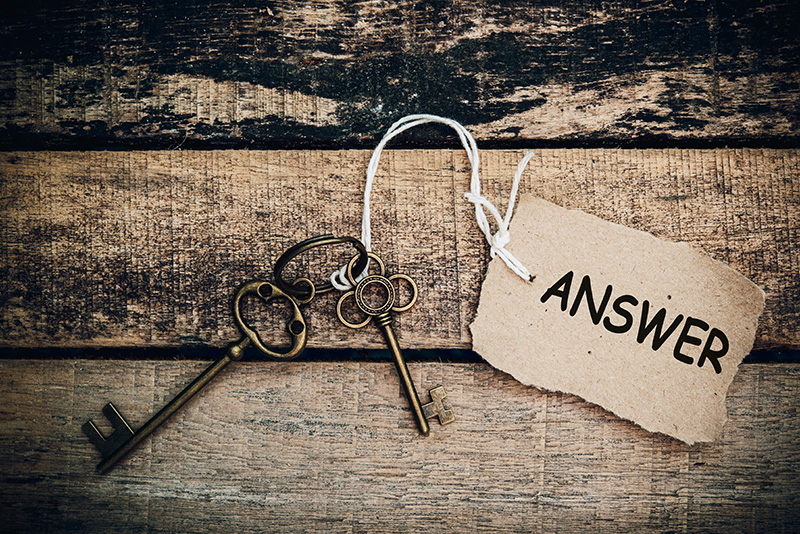 a set of antique looking keys on an old wood tabletop with a label with the word Answers attached to them with white string.