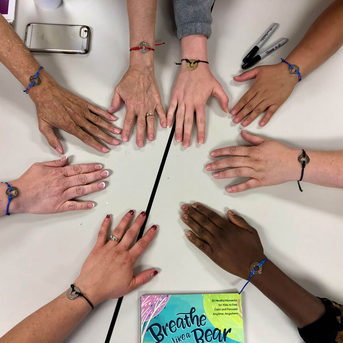 Group of adult hands placed together in a circle on a table.