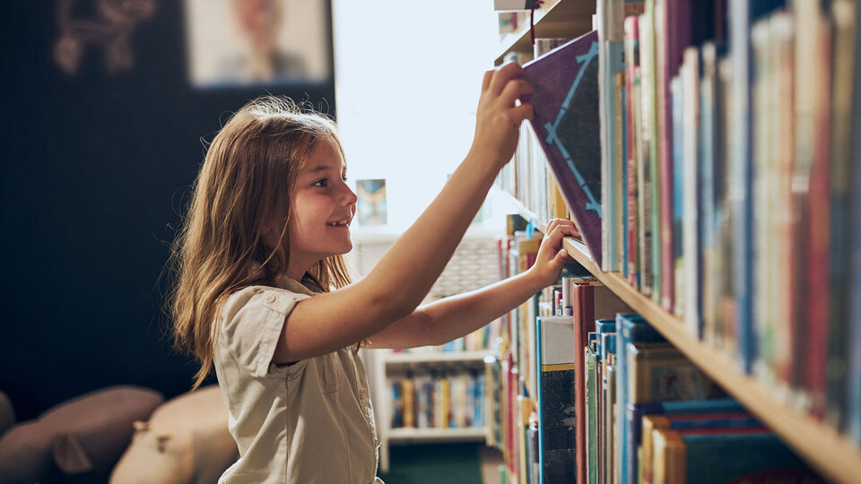 Girl getting a book from a bookshelf.