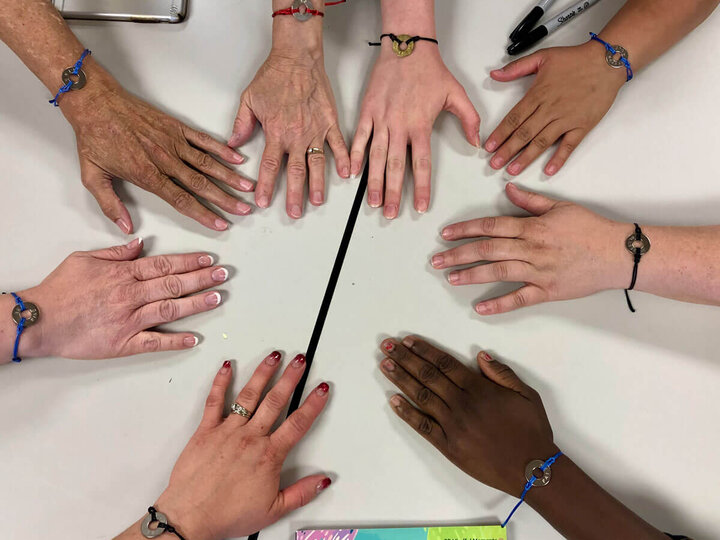 Group of adult hands placed together in a circle on a table.