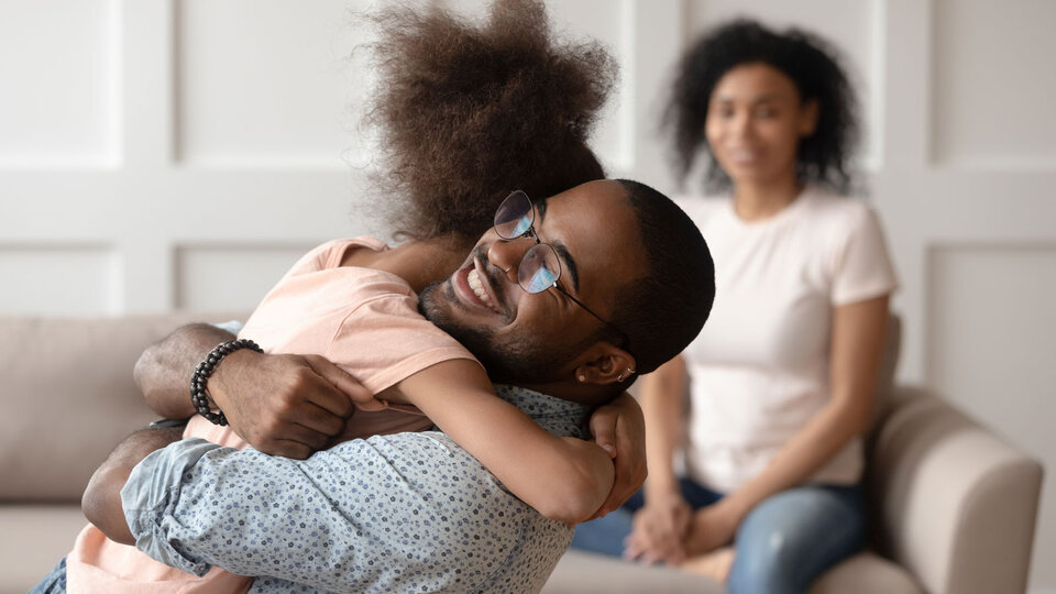Man hugging his daughter with woman looking on in the background.